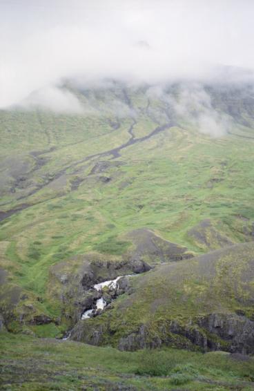 A waterfall running down below a mountain in low cloud